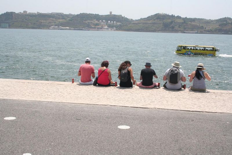 Touristen sitzend am Ufer des Tejo